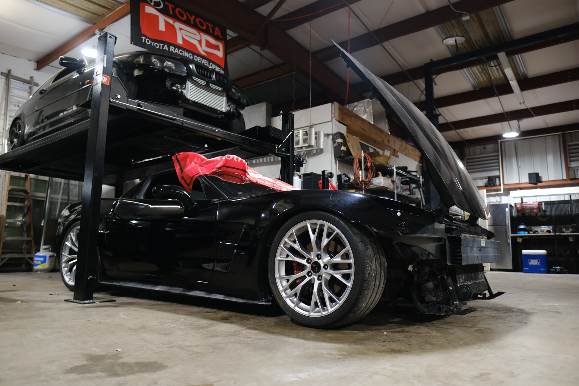 Corvette build with the hood off next to a turbo BMW on the stacked lift